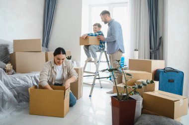 Mutlu bir aile taşınıyor, aileler ve çocuklar karton kutuları parlak bir odada birleştiriyor, yeni bir başlangıç için hazırlanıyorlar.