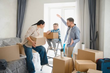 Karton kutular taşıyan mutlu bir aile, yeni dairede eşyaları boşaltıyor. Yeniden Yerleştirme Günü