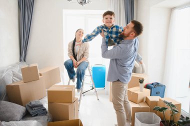 Mutlu aile yeni bir dairede karton kutuları açıyor, ebeveynler oğluyla oynuyor, yeni bir başlangıç için hazırlar.