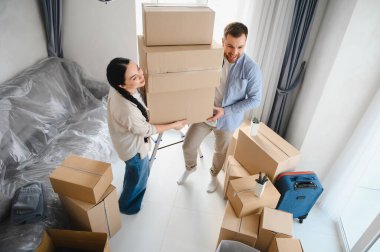 Karton kutular taşıyan, eşyaları boşaltan ve taşınırken yeni yaşam alanlarını döşeyen mutlu genç bir çift.