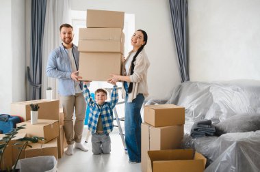Mutlu aile dairede karton kutuları açıyor. Ebeveynler ve çocuklar taşınma sırasında gülümsüyor, birlikte yeni bir hayata başlıyorlar.