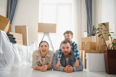 Mutlu bir aile taşınma gününde yeni evinde yerde karton kutularla çevrili yatıyor. Neşeli bir an, yeni bir başlangıç bekliyor