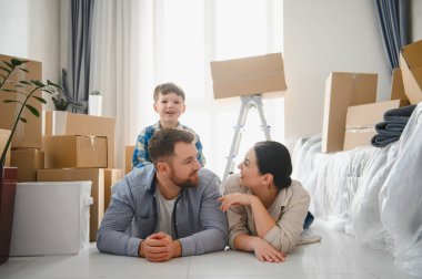 Mutlu aile dairede karton kutuları boşaltıyor, ebeveynler ve çocuklar taşınma gününde yeni eve taşınıyor.