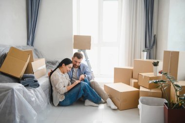 Oturma odasında, etrafı karton kutularla çevrili genç bir çift yeni bir evde yeni bir hayat planlıyorlar.