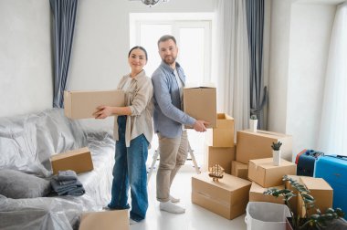 Mutlu çift sırt sırta durarak, yeni dairelerinde karton kutular taşıyorlar, taşınmak için gerekli malzemelerle çevrili.