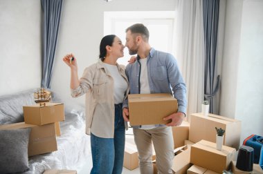 Mutlu çift dairelerine taşınıyor, karton kutuların arasında kucaklaşıyorlar, elinde yeni ev anahtarları tutan bir kadın.