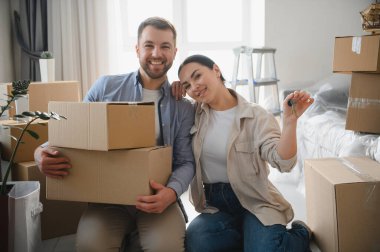 Gülümseyen genç bir çift ellerinde karton kutular ve yeni ev anahtarları, taşınma ve mülkiyet kutlamaları