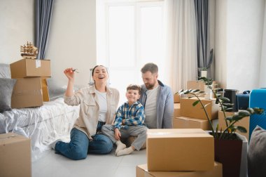 Aile yeni bir eve taşınıyor, aileler ve oğullar yerde oturuyor, mukavva kutuların arasında yeni başlangıçları kutluyorlar.