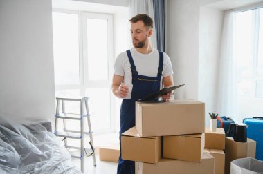 Karton kutuların arasında duran profesyonel bir nakliyeci, yeni bir ev taşınmasına hazırlanırken bir panoyu kontrol ediyor.