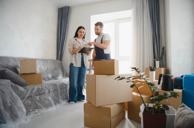 Karton kutularla çevrili dairede evrak işlerini yapan kadın ve nakliyeci, taşınmayı ve yeni başlangıçları sembolize ediyor.