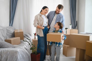 Mutlu aile yeni bir dairede karton kutuları açıyor. Aileler taşınma sırasında oğullarına bir kutu taşırken gülümsüyorlar.