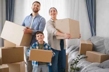 Yeni evlerinde yeni başlangıçlarını kutlayan karton kutular taşıyan ebeveynler ve oğullarla mutlu bir aile fotoğrafı.