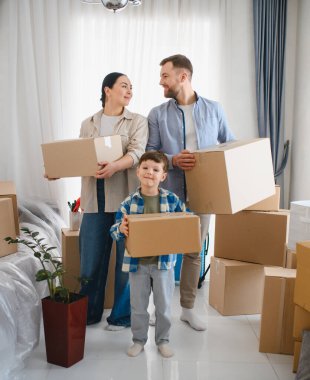 Yeni evlerine karton kutular taşıyan mutlu bir aile. Gülümseyen ebeveynler ve küçük oğullar yeni bir sayfa açıyorlar.