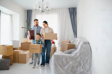 Mutlu aile, ebeveynler ve çocuklar, yeni evlerine kutular taşıyorlar, yeni bir evde yeni bir başlangıç yapıyorlar.