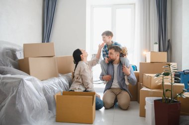 Mutlu bir aile yeni bir daireye taşınıyor. Ebeveynler ve çocuklar taşındıktan sonra karton kutularla çevrili. Mülkiyetin kutlanması ve başlaması