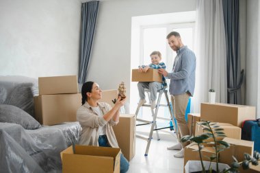 Mutlu aile kutuları açıyor ve yeni güneşli dairelerini dekore ediyor. Aileler ve küçük çocuklar gülümsüyor ve kaynaşıyorlar.