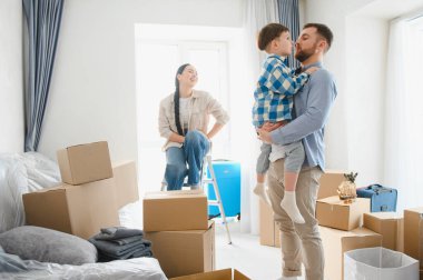 Genç aile, anne, baba ve oğul, kutuları açıyor ve yeni eve taşınmayı kutluyorlar.