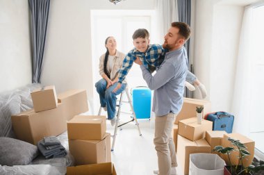 Mutlu bir aile yeni bir daireye taşınıyor, baba oğlunu kaldırırken anne izliyor, karton kutularla çevrili.