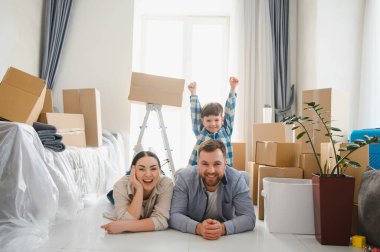 Genç, gülümseyen bir aile, taşınma günü boyunca mutluluk ve neşe içinde kutuları açıyor.