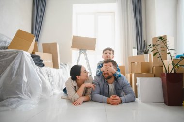 Ebeveynler ve çocuklar taşındıktan sonra karton kutularla çevrili yeni bir evin zemininde birlikte oynuyorlar.