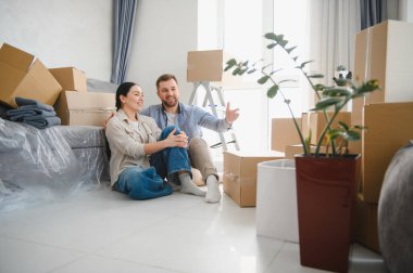 Genç çift yerde oturuyor, yeni evlerinin tadını çıkarıyorlar. Etrafı kutularla ve ev eşyalarıyla çevriliyken geleceklerini planlıyorlar.