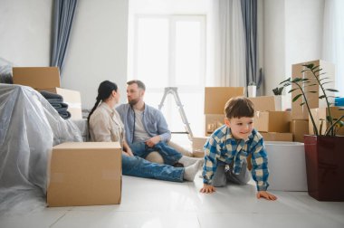 Mutlu bir aile dairede karton kutuları açıyor, yeni evlerine taşınmalarını küçük bir çocukla kutluyor.