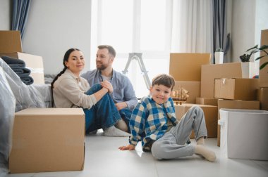 Aile yeni bir evde yeni başlangıçların tadını çıkarıyor. Ebeveynler ve çocuklar taşınma sırasında karton kutularla yerde dinleniyorlar.