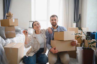 Mutlu çift yeni evlerine taşınmayı kutluyorlar. Etrafları kutularla çevrili ve ellerinde yeni ev anahtarları var.