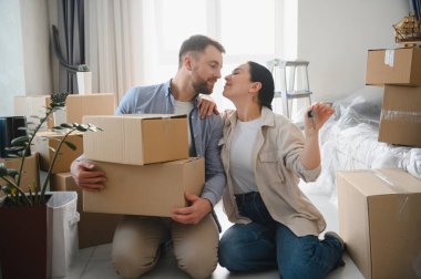 Genç çift taşınma gününü apartmandaki karton kutuları açarak kutluyorlar. Birbirlerine bakıyorlar. Evin anahtarlarını tutan kadın.