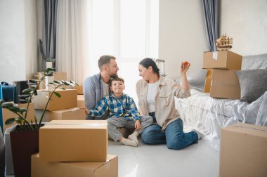 Yeni bir dairede karton kutuları açan mutlu bir aile. Yeni bir başlangıç ve gayrimenkul satın almaktan keyif alıyorlar.