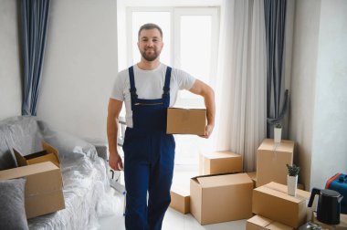 İş yerinde elinde karton bir kutu tutan bir adam taşınma günü boyunca paketlenmiş kutularla yeni bir evde duruyor.