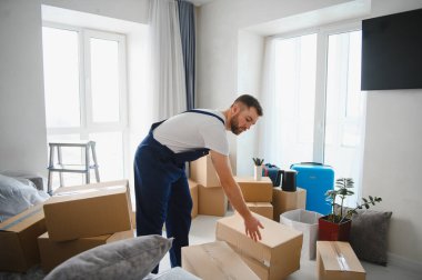 Profesyonel nakliyeci, boş bir odada karton kutular düzenliyor. Yer değiştirme, teslimat ve yeni bir başlangıcı simgeliyor.