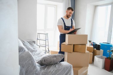 Teslimatçı, taşınma sırasında karton kutular ve paketlenmiş mobilyalarla panoya notlar yazıyor.