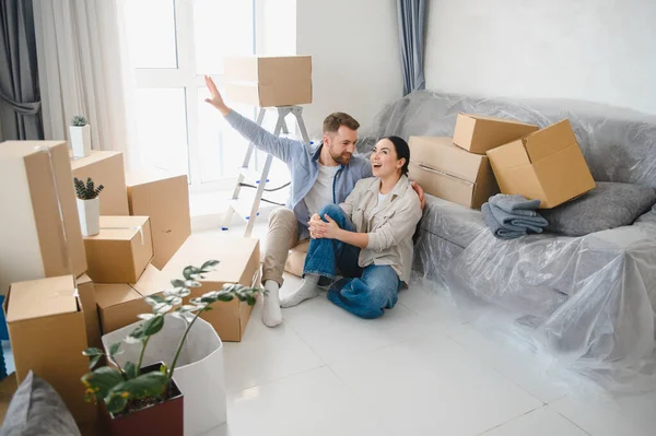 Genç çift yeni bir daireye taşınmayı kutluyorlar, karton kutularla çevrili yerde oturuyorlar ve mobilyalarla kaplılar.