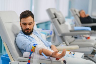 Sandalyede oturan genç bir adam, sakince, modern bir klinikte kan bağışlıyor. Hayati sağlık ve yardım konsepti