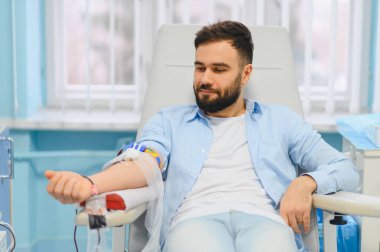 Modern kliniğe kan bağışı yapan bir adam, oturduğu yerden ve sakinken IV hastaları, kan naklini ve sağlık hizmetlerini desteklemek için kan topluyor.