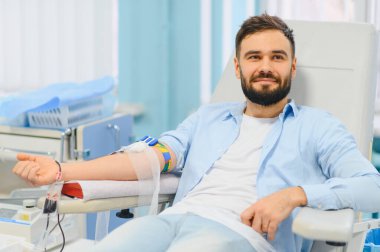 Genç bir adam klinik ortamda kan bağışı alıyor. Sağlığa katkıda bulunan ve hayat kurtaran bağışçı