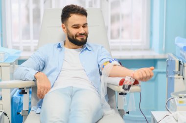 Genç adam kan verirken gülümsüyor, temiz bir klinik ortamında sağlık ve tıbbi desteğe katkıda bulunuyor