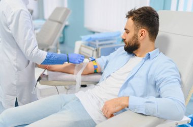 Tıp kürsüsünde yatan adam kan bağışlıyor, sağlık uzmanı kan topluyor, tıbbi yardım ve hasta bakımına katkıda bulunuyor.