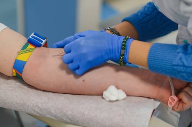 Donörün koluna iğne yapan mavi eldiven takan bir tıp çalışanı hastane prosedürü sırasında kan topluyor.