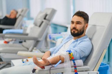 Klinik başkanlığında oturan genç adam kan bağışlıyor, sağlık hizmetlerine katkıda bulunuyor ve tıbbi tedaviyi destekliyor.