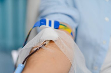 Kan bağışı sırasında kolunda serum olan kişi tüpü, iğneyi ve hayat kurtarmak için bakıcı desteğini göstersin.