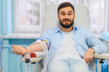 Kan bağışı sırasında gülümseyen, sağlık hizmetlerine katkıda bulunan ve fedakarlık gösteren bir adam.