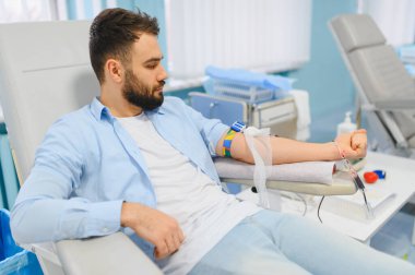 Tıbbi sandalyede oturan sakallı bir adam. İşleme odaklanırken kan bağışlıyor. Fedakarlık ve sağlık konsepti