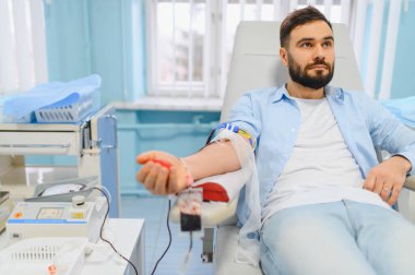 Temel bir tıbbi prosedür sırasında klinik koltuğunda kan vererek sağlık hizmetlerine katkıda bulunan bir adam.