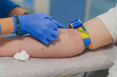 Sağlık uzmanı kan örneği alıyor, turnike uyguluyor ve klinik ortamında venipunktur için hazırlanıyor.