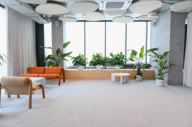 Tavanda turuncu bir kanepe, saksı bitkileri ve ses emici akustik paneller bulunan parlak, minimalist ofis salonu.