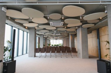 Boş modern konferans odası sandalye, projektör, akustik tavan panelleri ve tam uzunluktaki pencereleri gösterir