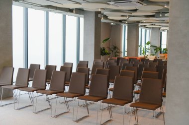 Büyük pencereli, parlak, çağdaş bir toplantı alanına kurulmuş kahverengi sandalyeler kurumsal bir toplantıya veya sunuma hazır.