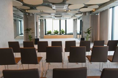 Minimalist tasarım, büyük pencereler ve akustik tavan panelleri içeren, sahneye bakan sandalyeli boş modern konferans odası